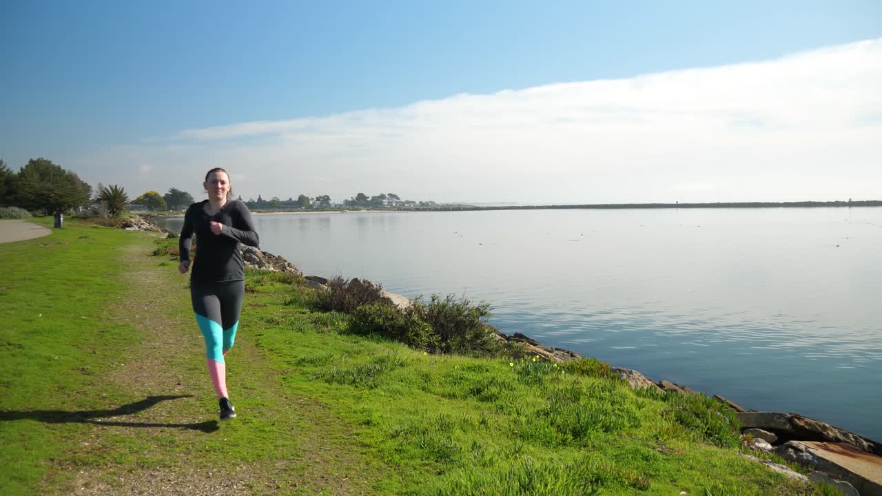 Young girl runs toward and past camera on a flat grassy lakeside path