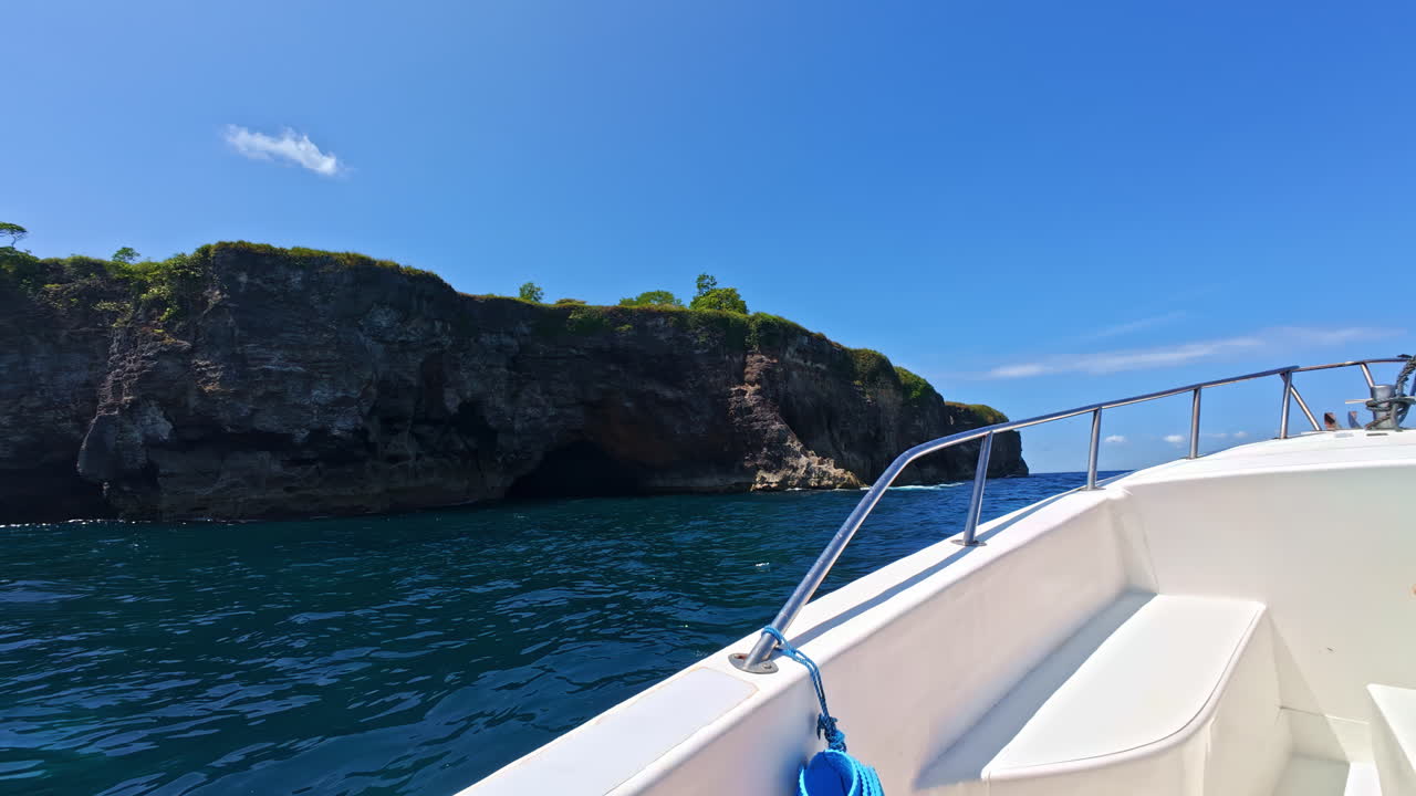 Vista da motoscafo diretto verso un’isola rocciosa lussureggiante su un mare blu intenso. Nusa Penida, Indonesia