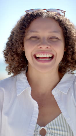 vertical video: smiling woman enjoying sunny day at beach, wearing sunglasses on head