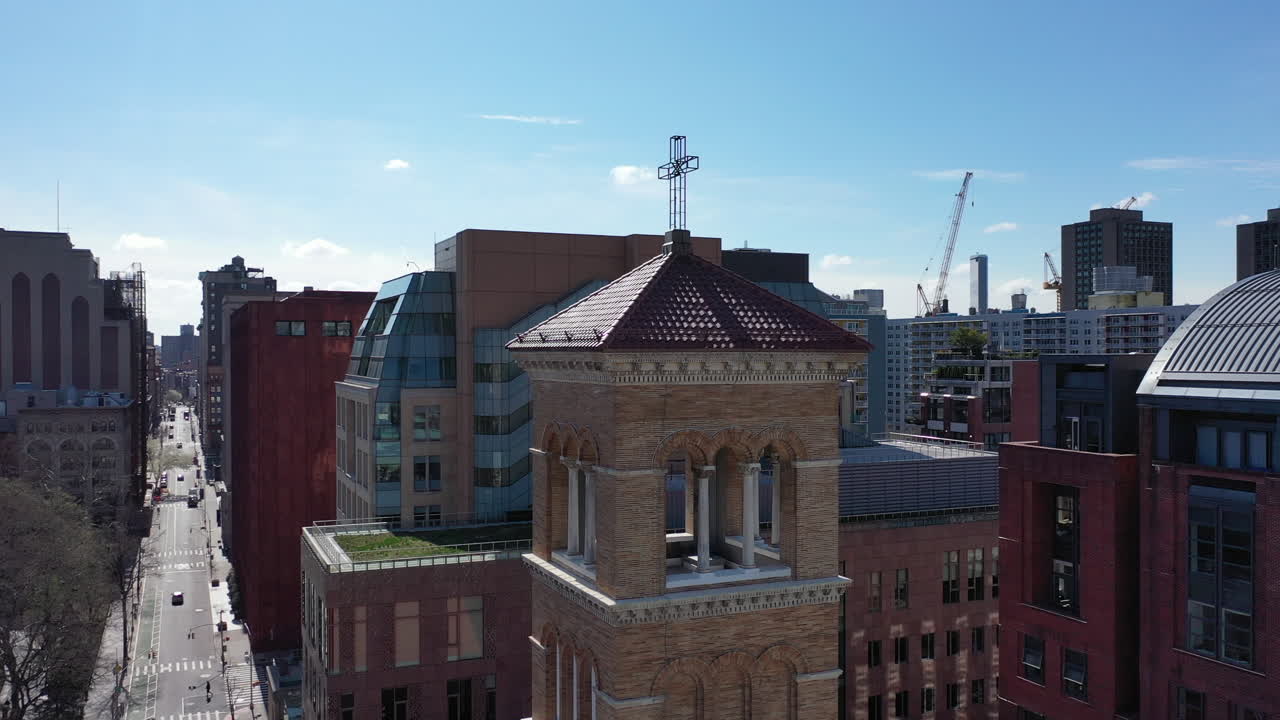 an aerial view over the bell tower of a church in Greenwich Village, NYC. The drone camera orbit counterclockwise around the red roof tower on a sunny day. The Freedom Tower is in the distance.
