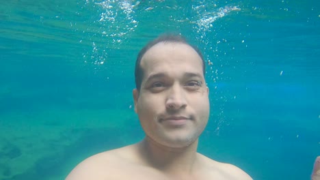 young man swimming in blue clear under water of waterfall with many rocks from flat angle