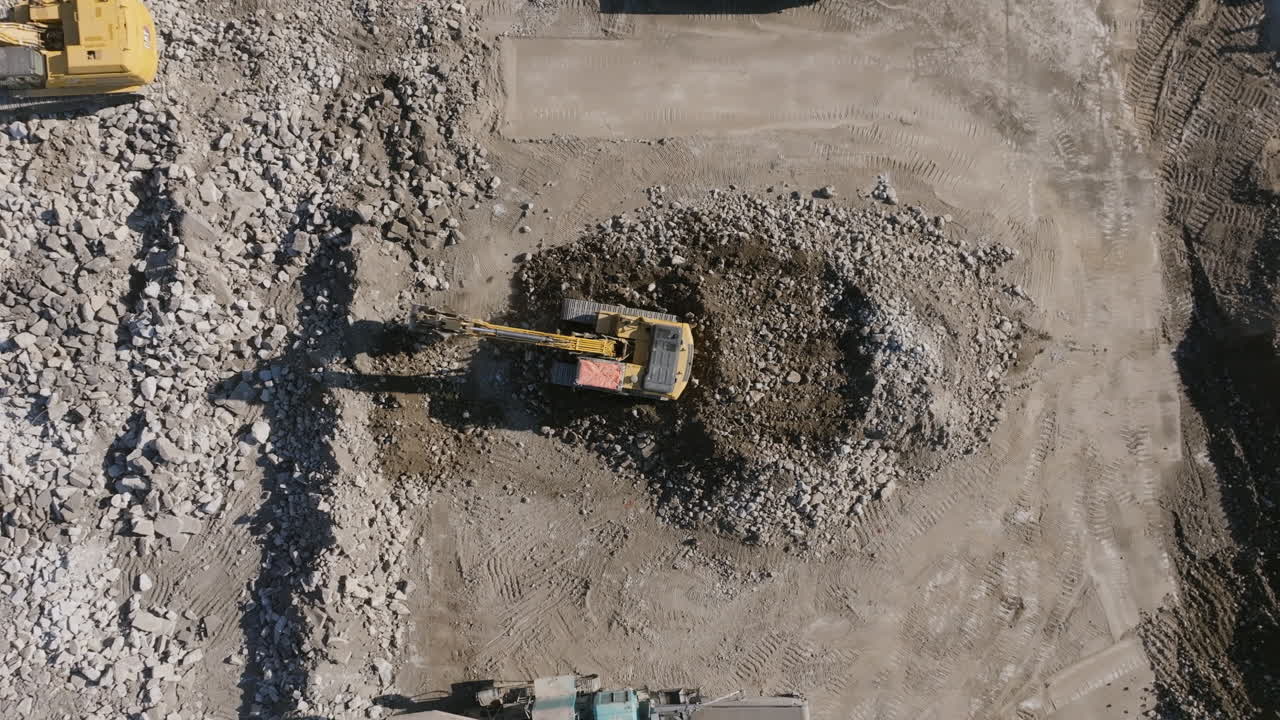 imágenes aéreas estáticas de una excavadora que mueve rocas en un sitio de construcción.