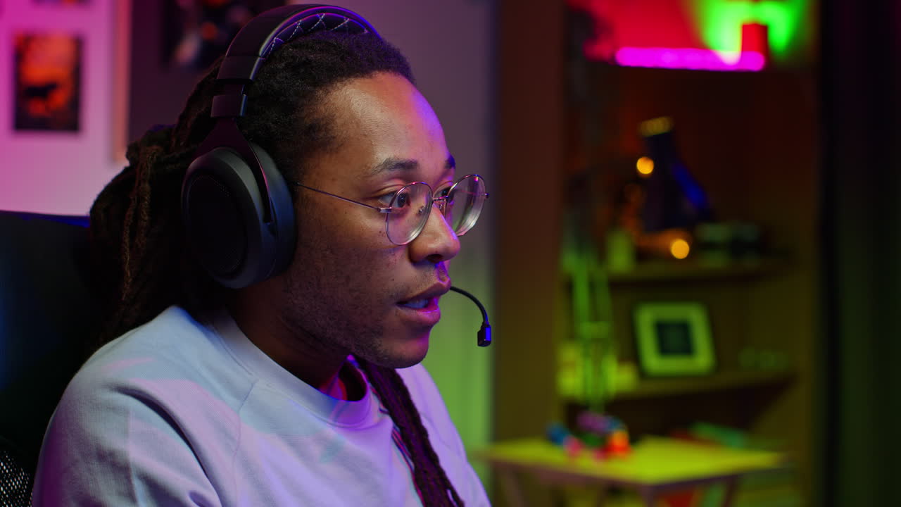 A young man with headphones and a microphone is playing a video game. He is focused and determined.