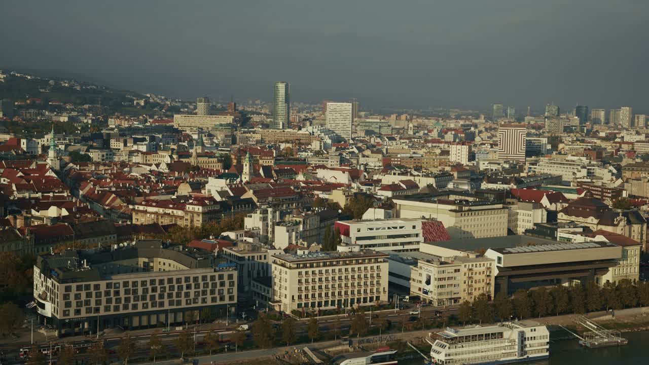 Bratislava skyline with red rooftops, modern buildings, and hills in warm sunlight