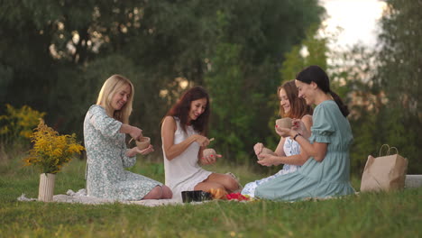 a group of young beautiful women in nature in an open area sculpt from clay use tools decorate products communicate share impressions laugh rejoice at the results. a common hobby.