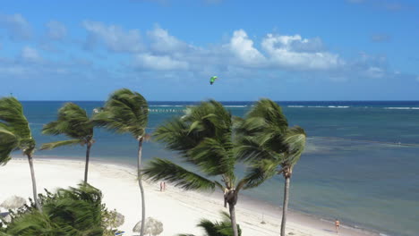 Parapente-Sobre-El-Mar-Con-La-Costa-Tropical-De-La-Playa-De-Palmeras,-Tiro-Largo-De-Drones