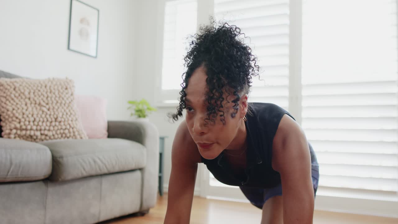 African American woman in workout starting tabletop holding plank bracing core at home near sofa
