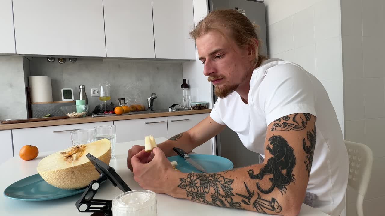 Junger Mann isst frische Melone in einer modernen Küche