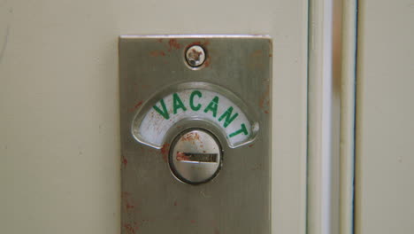 slow motion close-up of bathroom stall lock changing from "vacant" to "engaged