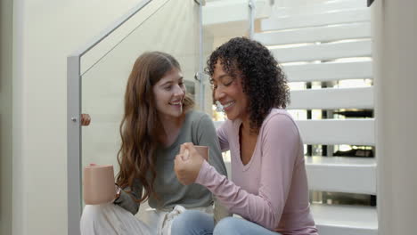 sitting on stairs, lesbian couple enjoying coffee and smiling at home