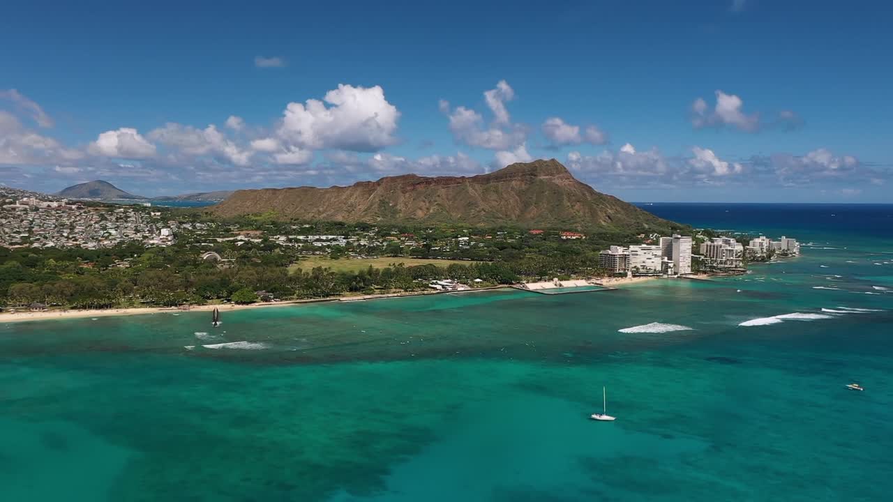 Aerial drone view showing Waikiki Beach with turquoise ocean water, Diamond Head crater, and Honolulu cityscape on Oahu Island under bright blue sky in Hawaii
