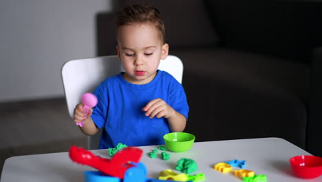 adorable little kid sits at desk playing with plasticine. lovely boy playing peacefully at home. blurred backdrop.