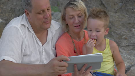 madre y hijo viendo video en la tableta mientras están sentados en la playa