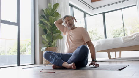 senior biracial man practicing yoga meditation at home, slow motion