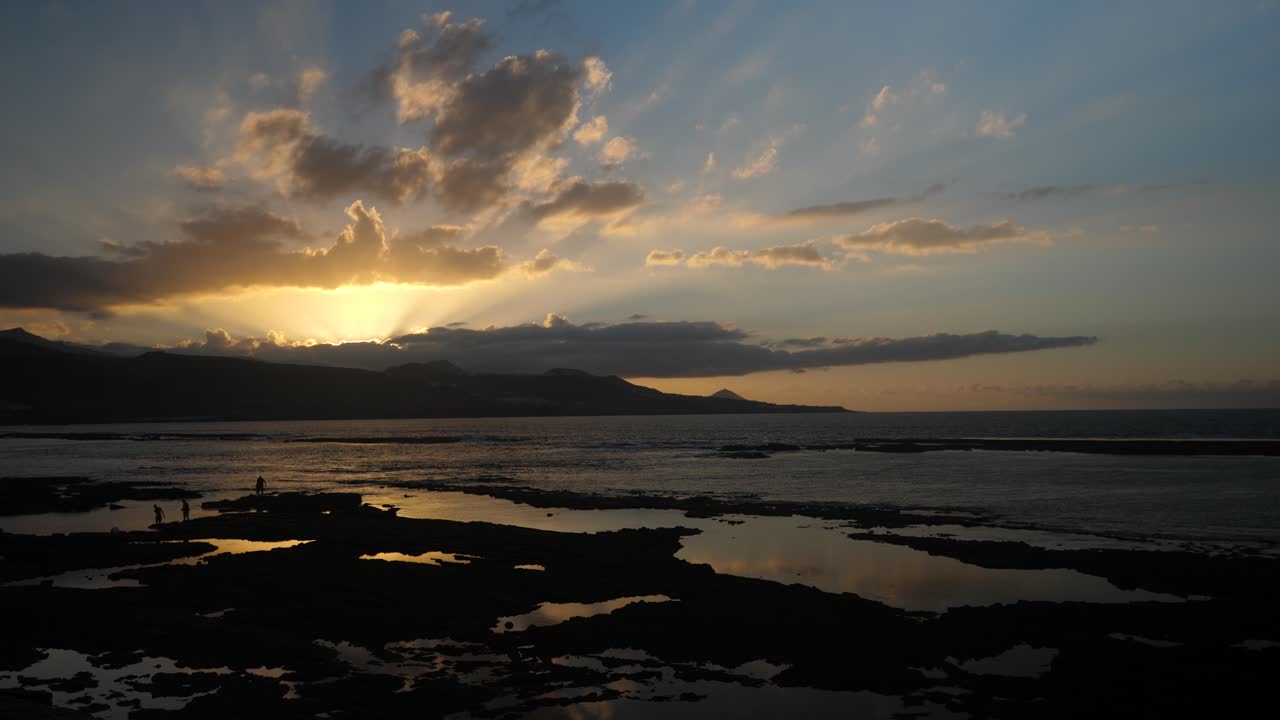 Dramatic Sunset Over Rocky Ocean Coastline with Distant Mountains
