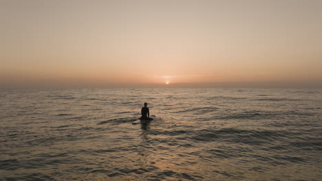 surfer-girl-paddeling-into-sunrise-then-sitting-on-surfboard-and-wath-the-sun-on-fuerteventura-Canary-Islands