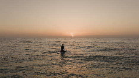 Chica-Surfista-Remando-Hacia-El-Amanecer-Y-Luego-Sentada-En-Una-Tabla-De-Surf-Y-Viendo-El-Sol-En-Las-Islas-Canarias-De-Fuerteventura