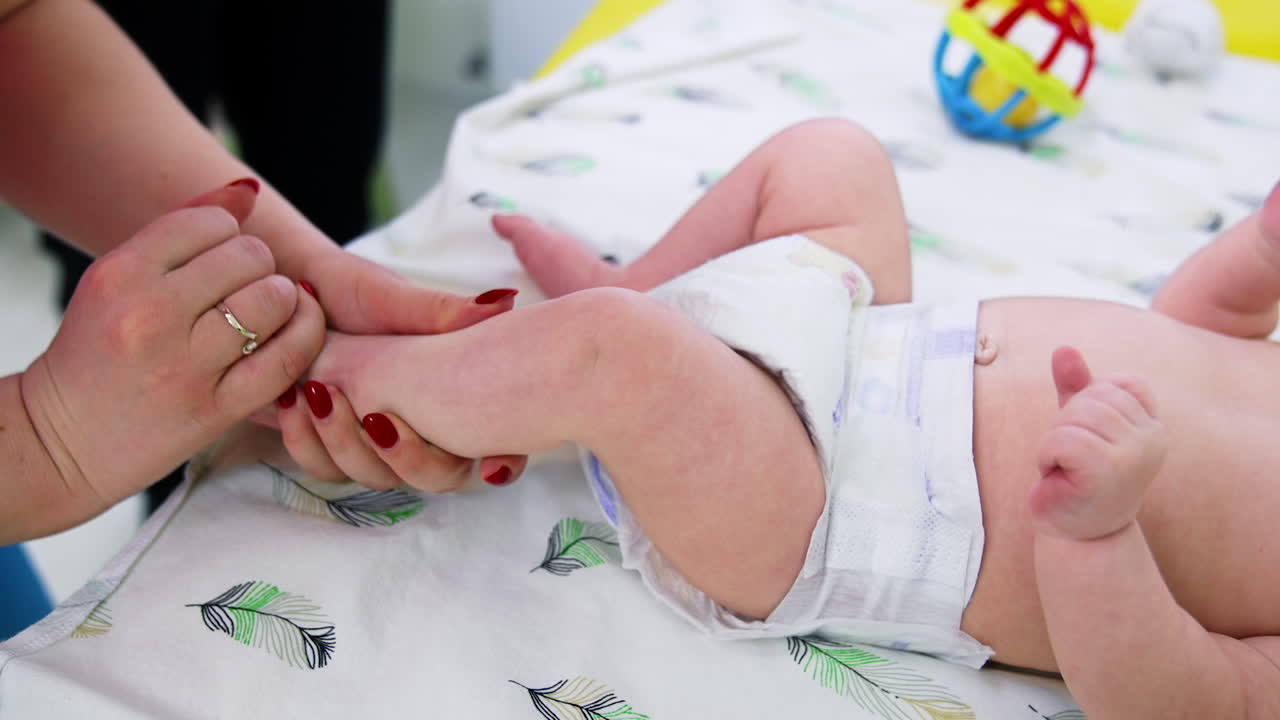 Doctor is checking the toddler's development. Female pediatrician turning baby's foot and checks the leg. Close up.
