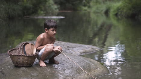 kid sitting on a rock at the river playing with a stick