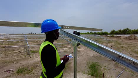 black african engineer wearing blue helmet taking measurements of solar panel array beam structure tilt angles