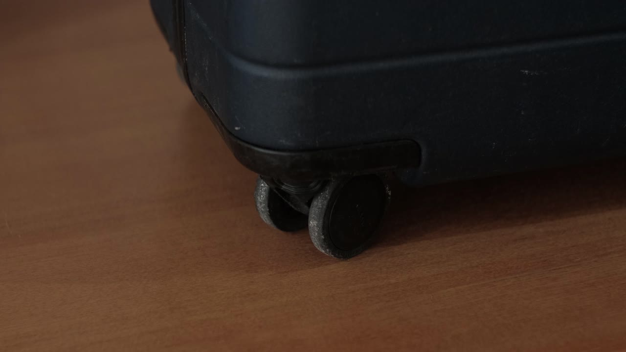 Primer plano de ruedas giratorias de una maleta de equipaje resistente con carcasa sobre una superficie de madera