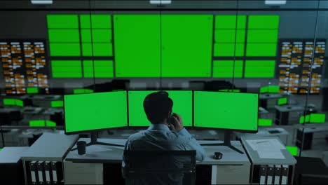vista trasera de un hombre asiático hablando en el teléfono móvil mientras trabajaba con múltiples monitores de computadora simulados en la oficina