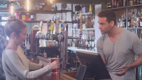 female customer in bar makes socially distanced contactless payment for drinks in health pandemic