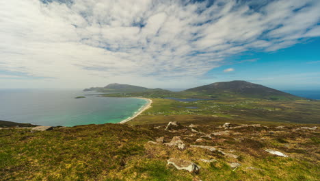 Timelapse-of-seaside-remote-bogland-village-with-sand-beach,-grass-and-rocks-with-clouds-casting-shadows-on-sunny-day-viewed-from-Minaugn-Heights-in-Achill-Island-in-county-Mayo-in-Ireland