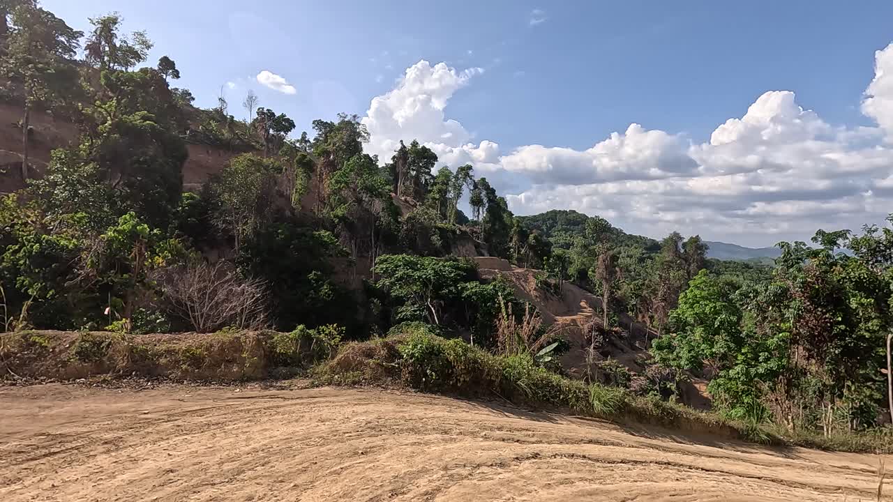 A vehicle navigates a winding dirt road through lush, hilly terrain under bright daylight in Phuket, Thailand