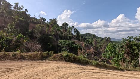 a vehicle navigates a winding dirt road through lush, hilly terrain under bright daylight in phuket, thailand