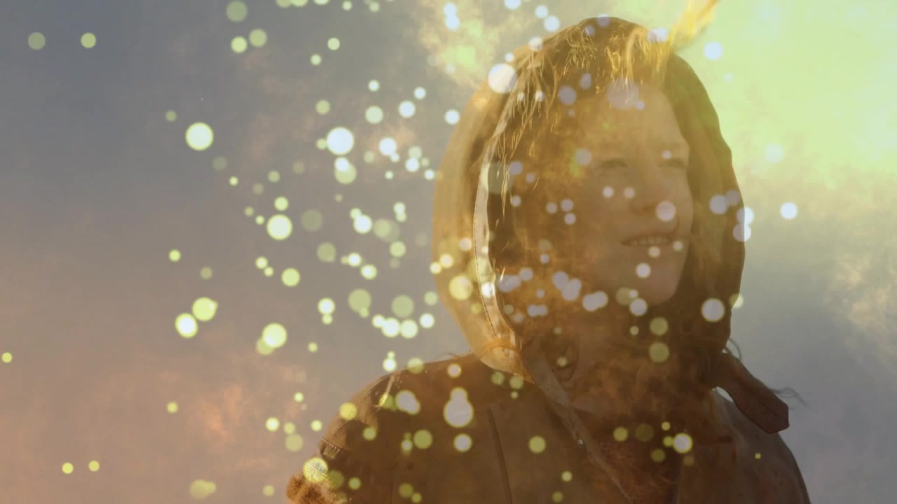 Mujer con capucha girando hacia el sol mientras un bokeh dorado se desplaza sobre su rostro, revelando una suave sonrisa, marketing