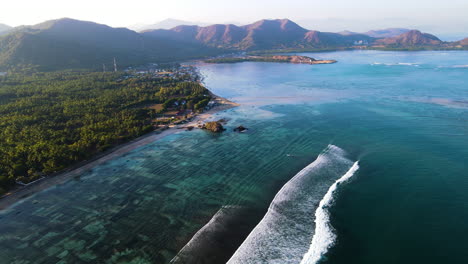 calm waves on forested shoreline with mountain background in indonesia. aerial drone shot