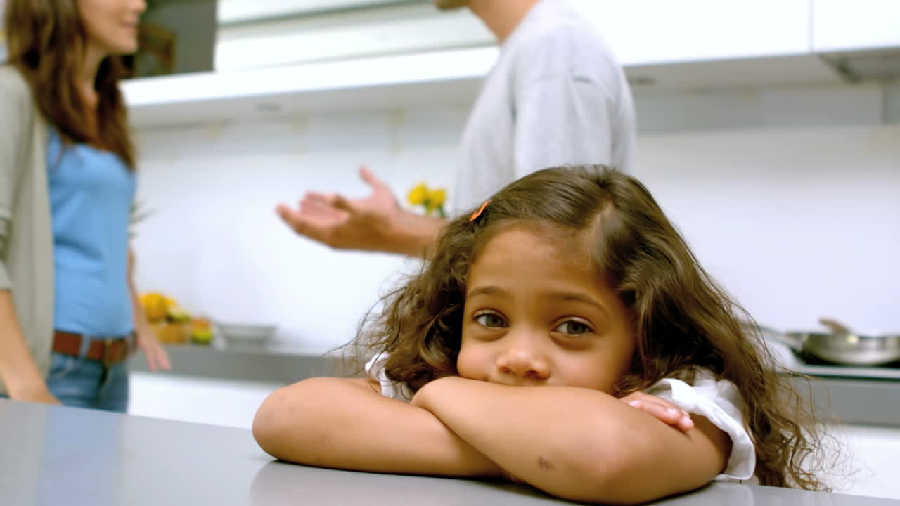 niña triste con los brazos cruzados mientras los padres pelean