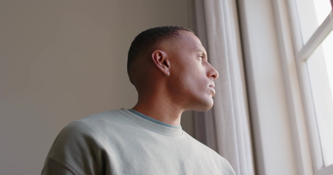 Adult African American man turning, window light pulling gaze, scanning outside wearing crewneck
