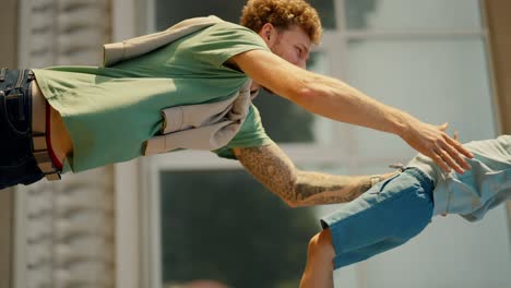 vertical video: a happy little blond boy in blue clothes with a blue backpack runs from school to his dad who takes him in his arms, they are very happy to meet