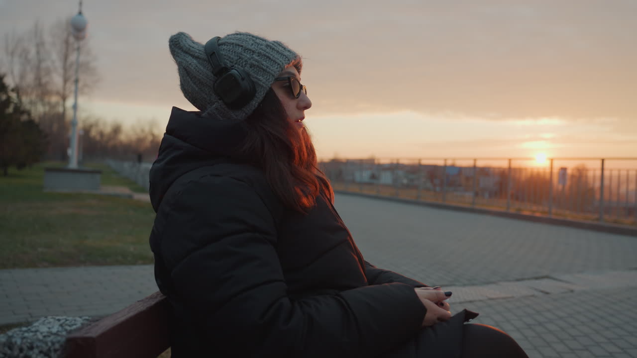 Žena si užívá hudbu během klidného večerního tance. Klidná žena ladně tančí za soumraku v městském parku. Klidná ženská postava se pohupuje do melodických tónů na pozadí městské scenérie západu slunce.