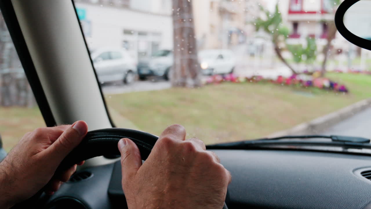 Close up of a man's hands on a steering wheel, driving a car on the road