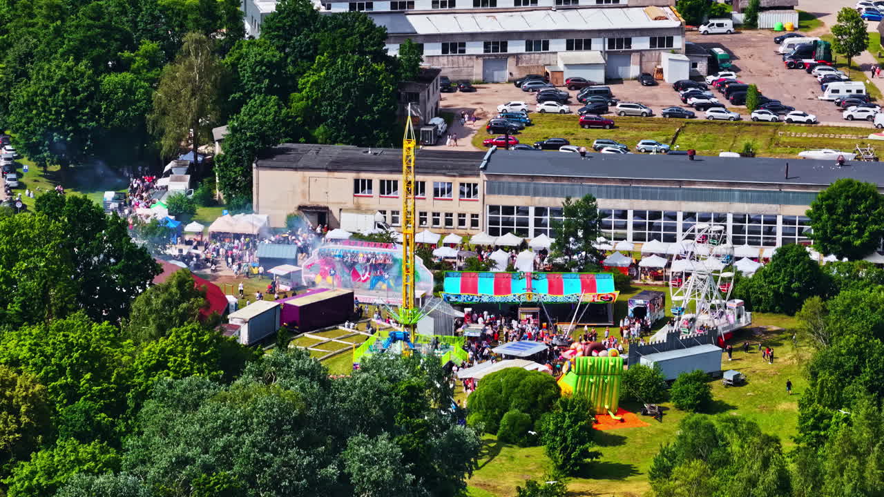 Ein lebhaftes Sommerfestival füllt das Stadtzentrum mit Fahrgeschäften, Buden, Menschenmassen und leuchtenden Farben, aus der Vogelperspektive während der Zvejnieksvētki-Feier in Engure aufgenommen.