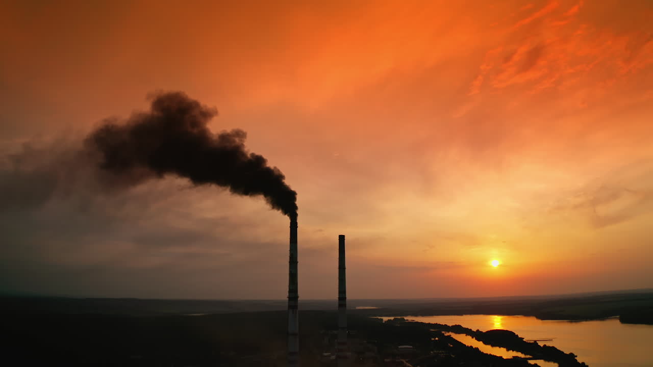 Drone shot flying over facility. Aerial view of factory with smoke at sunset