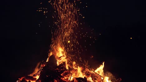 burning fire with logs and coals at night. bright sparks and heavy smoke from the fire. a man turns firewood with a pitchfork.. burning branches in the fire, tongues of flame