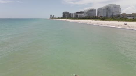 aerial: lone young woman swims to shore at surfside beach, miami