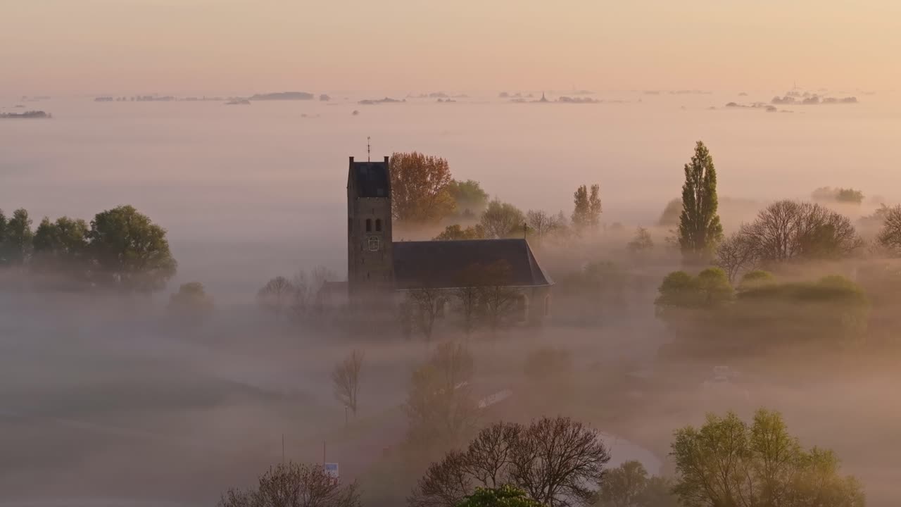 Aerial view of quiet Hichtum with church and water veiled in dawn mist