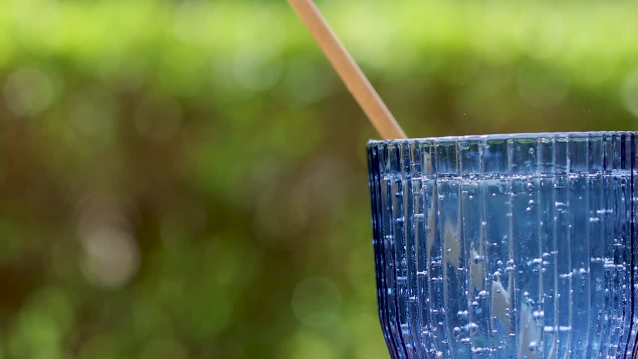 Close-up shot of a hand inserting a biodegradable straw into a blue textured water glass