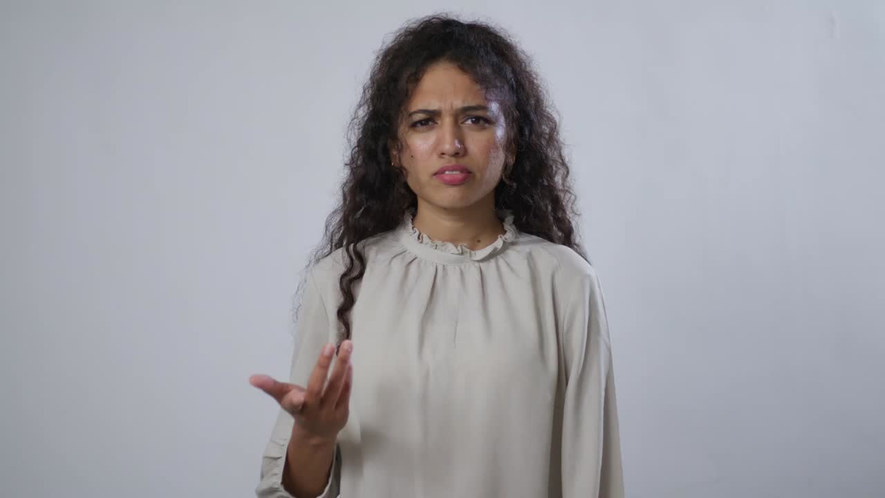 A South Asian woman with curly brown hair looks confused and frustrated, gesturing with her open palm