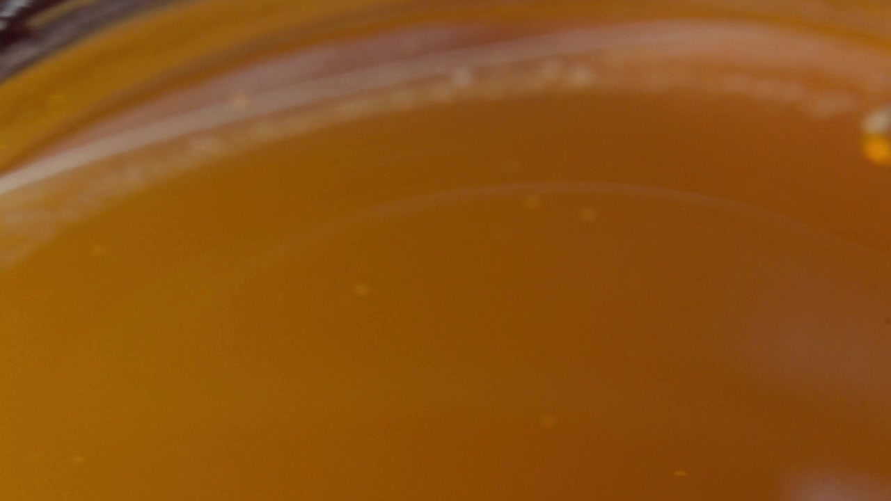 Primo piano panoramico di miele dorato all'interno di un barattolo di vetro, che mostra una superficie liscia e lucida, un ricco colore ambrato e una consistenza naturale densa in una vista macro dettagliata con riflessi caldi.