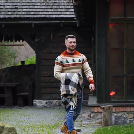 man walks out a wooden house with big blanket in hands. autumn evening outside