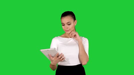 mujer joven atractiva o estudiante que lee información en una tableta en una pantalla verde, tecla de croma
