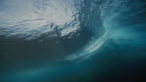 underwater sideview of surfer riding and carving into top of wave at cloudbreak fiji