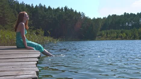 una mujer relajándose, sentada al lado de un embarcadero salpicando sus pies en el agua de un río-lago