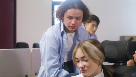 happy boy sitting on table and talking with his female collegue who sitting on chair and using mobile phone during a party in the office